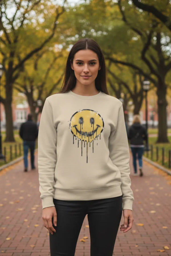 Woman wearing a beige sweatshirt with a yellow smiley face design outdoors.