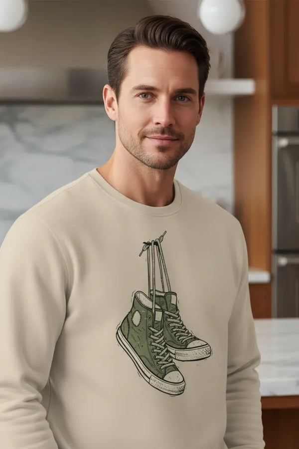 Man wearing a beige sweatshirt with a graphic design of green sneakers in a kitchen setting