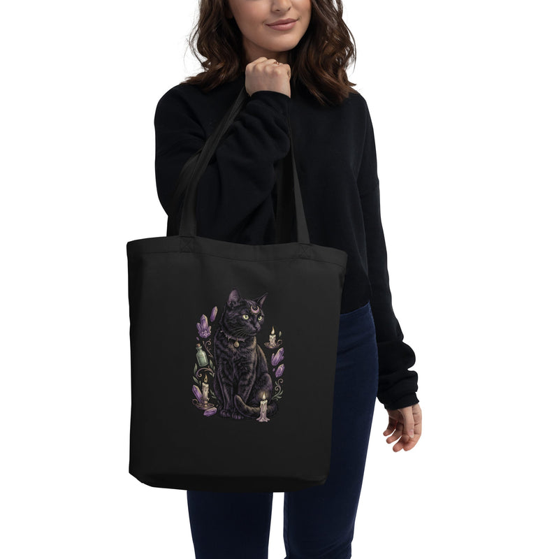 Woman in black sweatshirt holds a black tote bag with a mystic cat graphic.