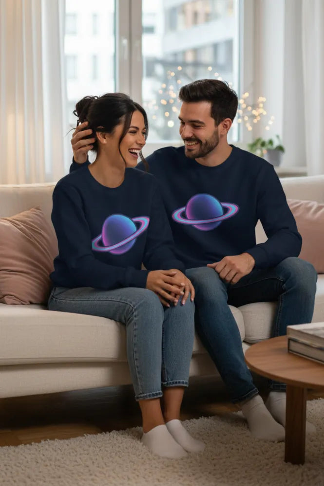 A smiling couple wearing matching navy sweatshirts with a neon planet graphic, sitting on a cream sofa.