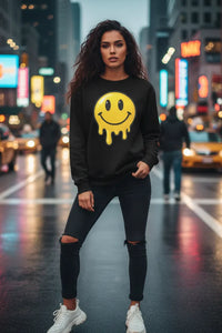 Woman wearing a black sweatshirt with a yellow smiley face design on a city street at night.