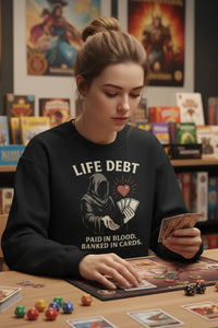 Person wearing a black sweatshirt with a graphic design and text, sitting at a table with board games and cards.