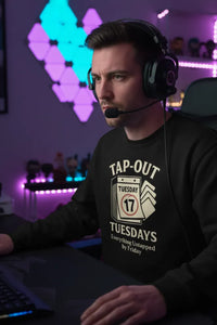 Person wearing a black sweatshirt with 'Tap Out Tuesday' text in a gaming setup with colorful lights.