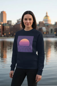 Person wearing a black sweatshirt with a colorful graphic design, standing by a waterfront with buildings in the background.
