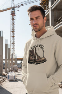 Man wearing a beige hoodie with a graphic design of boots and text 'Walk a Mile' at a construction site.