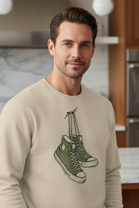 Man wearing a beige sweatshirt with a graphic design of green sneakers in a kitchen setting