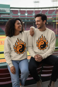Two people sitting on a bench wearing matching sweatshirts with fire and yin-yang symbols.