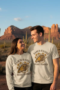 Two people wearing 'Ranch-Raised Heart-Forced' shirts in a desert setting with mountains and cacti.